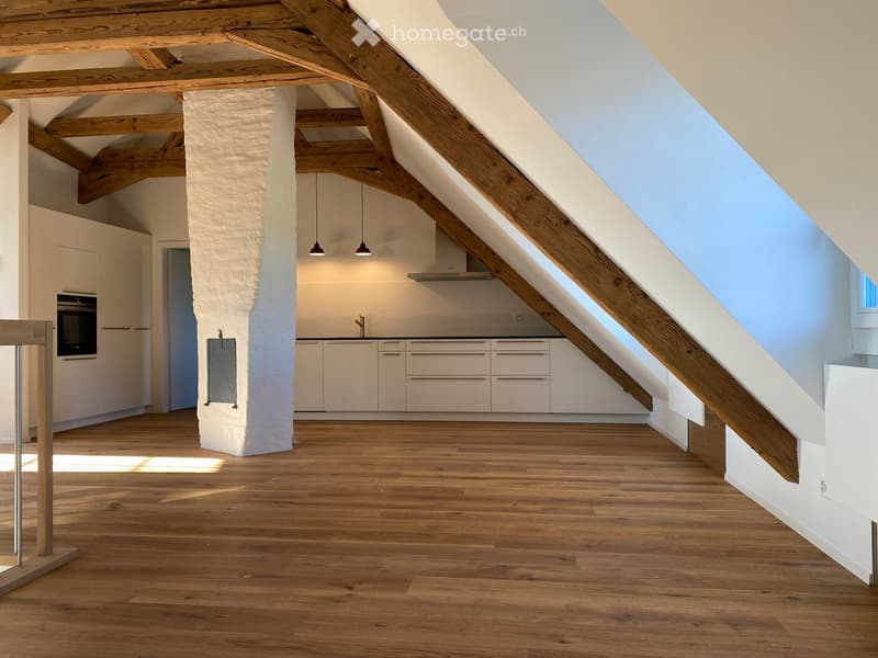 Open-plan attic space with wooden beams, light-colored cabinets, and a modern kitchen area.
