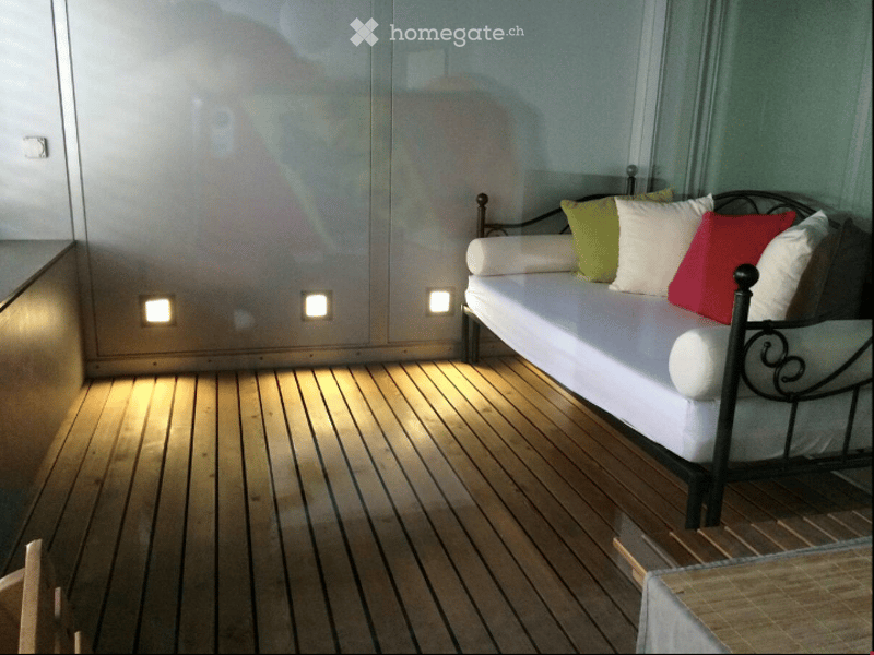 Cozy balcony with wooden decking, white sofa, and colorful pillows.