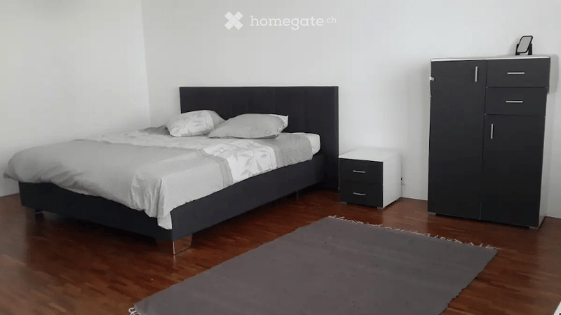 Modern bedroom with a dark wooden bed, white bedding, a nightstand, a wardrobe, and a grey rug on the floor.