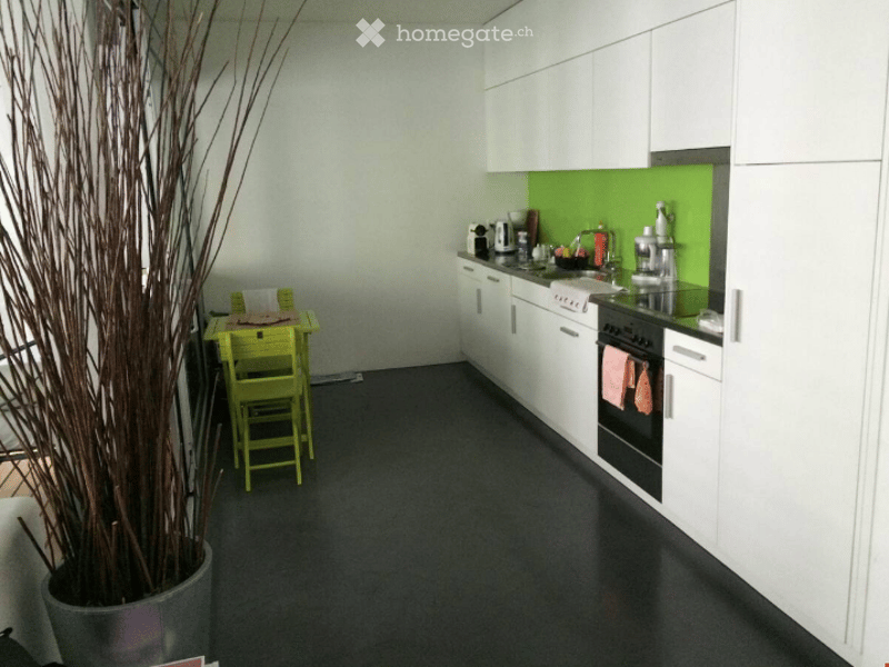 Modern kitchen with white cabinets, black countertops, and a green backsplash. Includes a small yellow table and chairs, a potted plant, and various kitchen appliances.