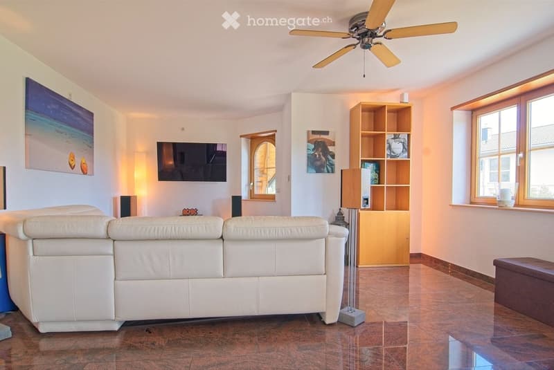 Modern living room with white leather sofa, wooden shelf, table lamp, floor lamp, television, and a ceiling fan.