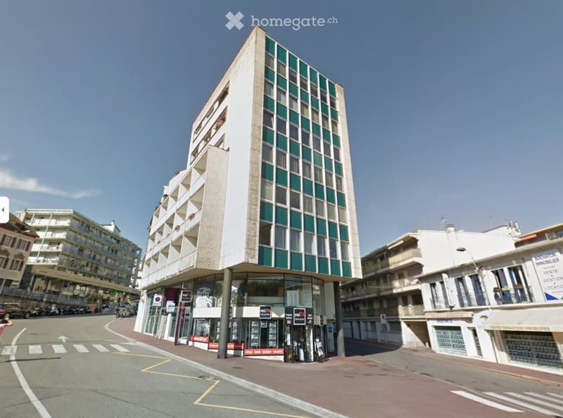 A modern multi-story building with a mix of glass and concrete facade, located on a street corner with adjacent buildings and signage.