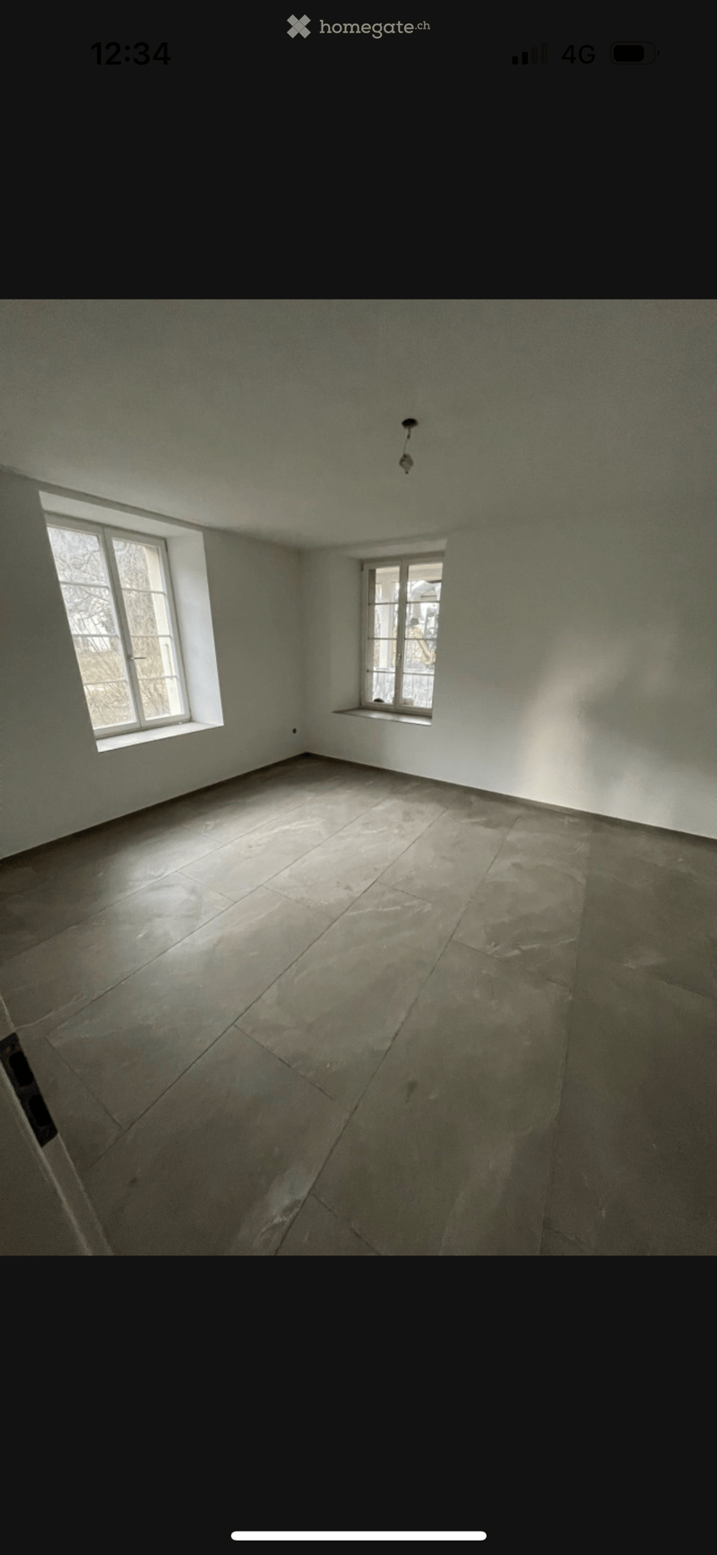 Empty room with bare walls and a concrete floor, featuring two windows allowing natural light to enter.