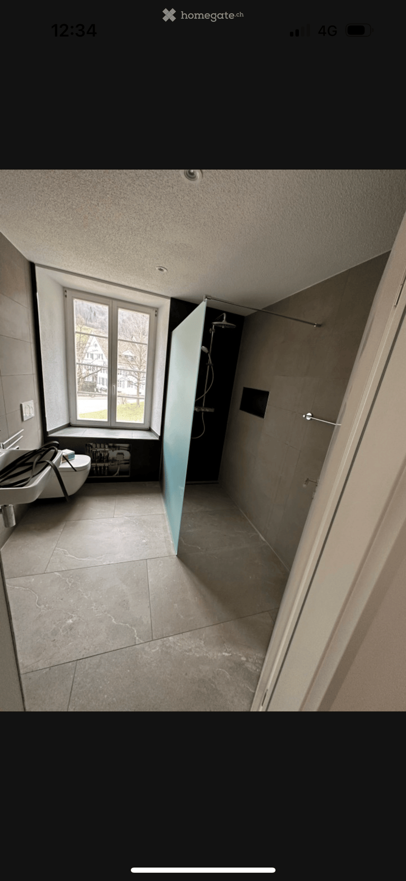 Modern bathroom with tiled floor, large window, sink, toilet, and separate shower area with glass door.
