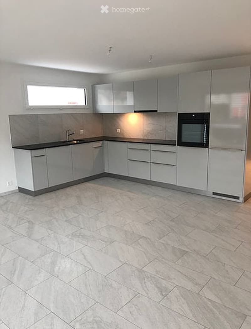 Modern, minimalist kitchen with grey cabinets, a black countertop, and a large window. Features a sink, faucet, and microwave.