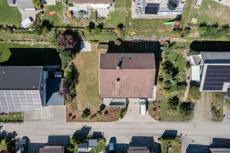 Aerial view of a residential area with multiple houses, gardens, driveways, and parked cars.