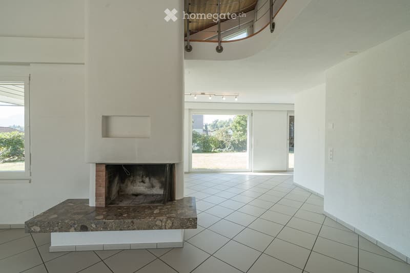 An unfurnished room with a fireplace, white tiled floor, large windows, and a curved staircase leading to an upper level.