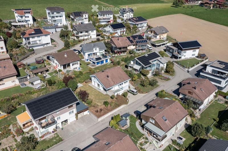 Aerial view of a residential neighborhood with multiple houses, solar panels on roofs, driveways, and surrounding greenery.