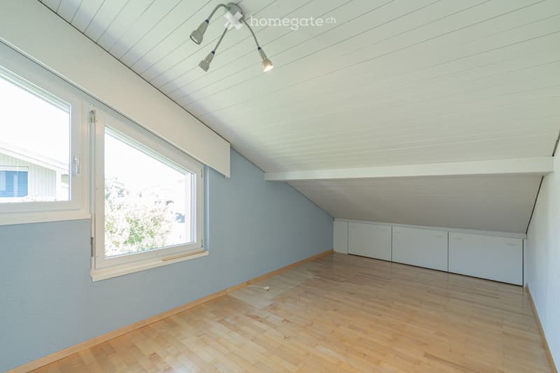 Empty room with wooden flooring, light blue walls, white cabinets, and large windows allowing natural light.