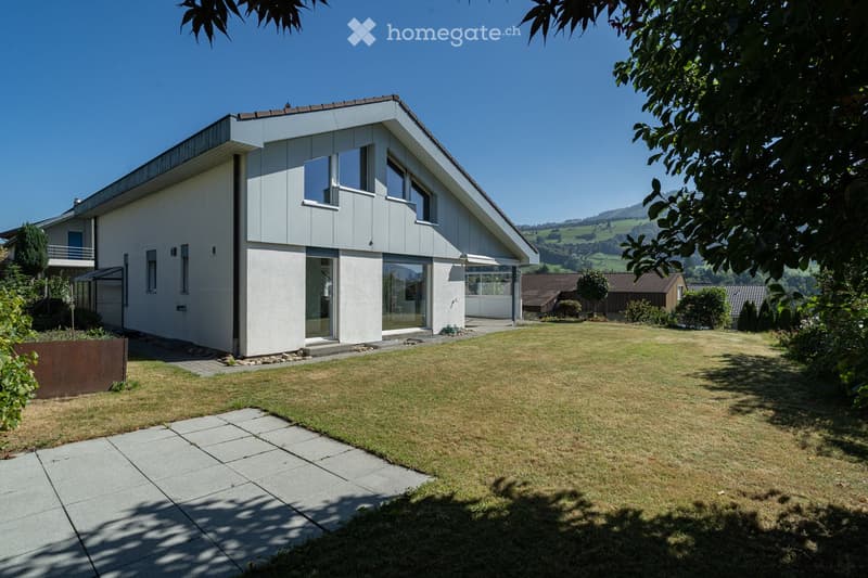 Modern two-story house with white exterior, large windows, and a spacious lawn in front.