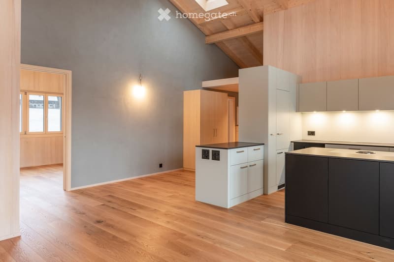 Modern kitchen with light grey walls, wooden flooring, white cabinets, and a dark grey island.