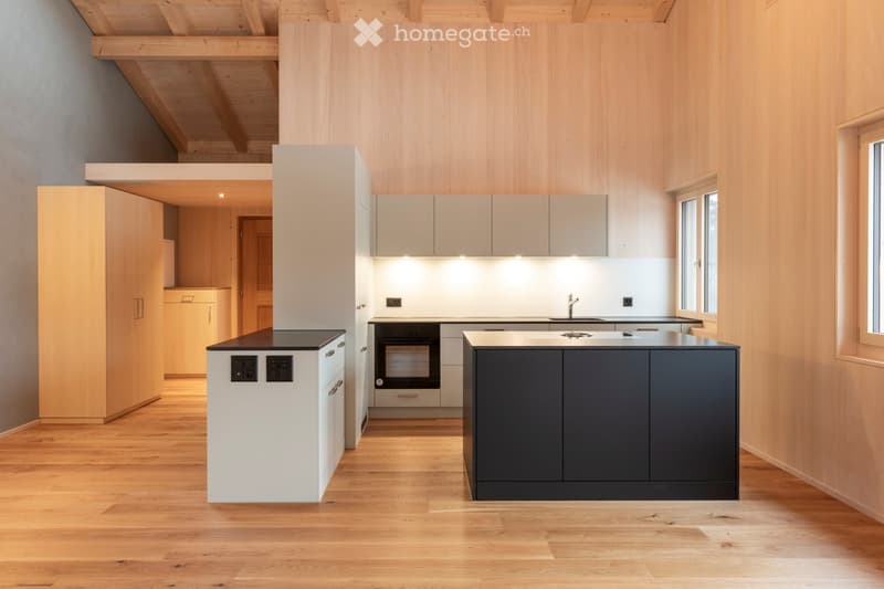 Modern kitchen with light wood walls, white cabinets, dark countertops, and a central island. Features an oven, sink, and faucet.