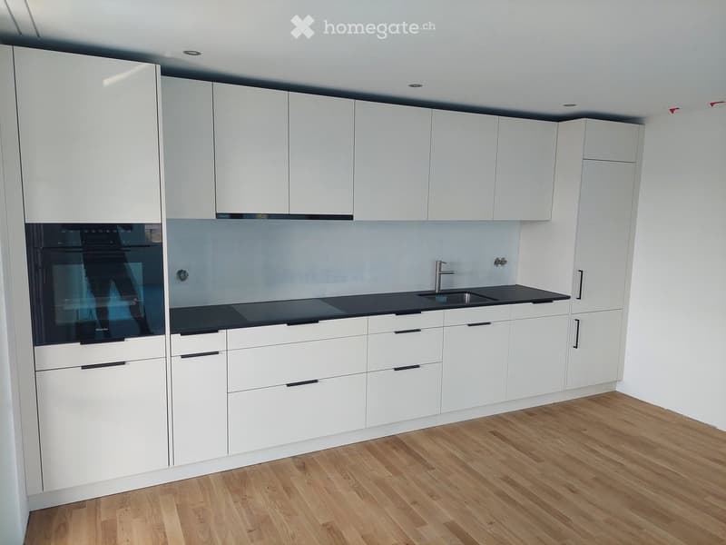 Modern kitchen with white cabinets, black countertops, and a built-in oven. Features a sleek design with a wooden floor and integrated sink and faucet.