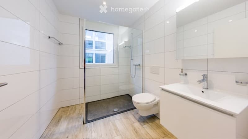 Modern bathroom with white tiles, a glass-enclosed shower, a toilet, a sink with a modern faucet, and a large mirror above the sink.