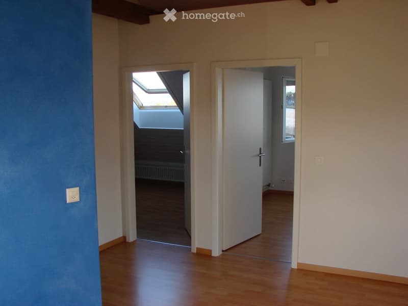 Empty room with wooden flooring, white walls, and two doors leading to other spaces. One door opens to a room with a window, and the other leads to a space with a skylight.