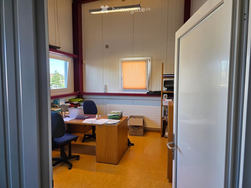 Office space with a wooden desk, office chair, laptop, shelves, and a door leading to another room.