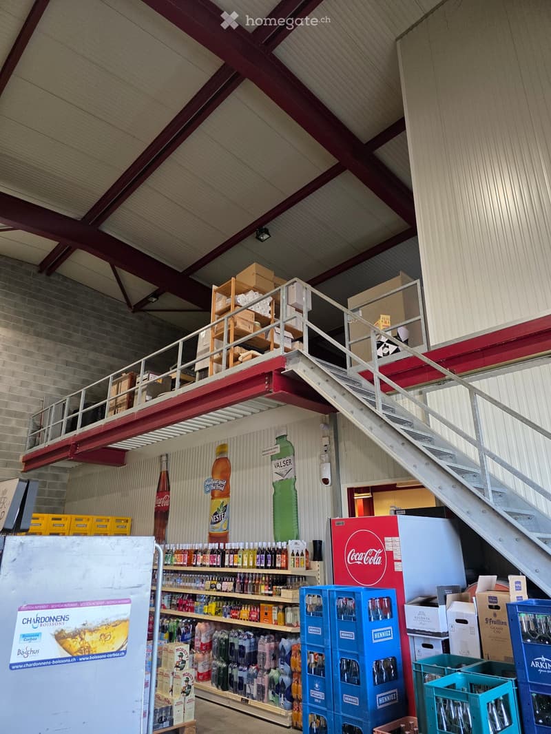 Warehouse or storage area with shelves stocked with various beverages, a staircase leading to an upper level, and storage boxes scattered around.
