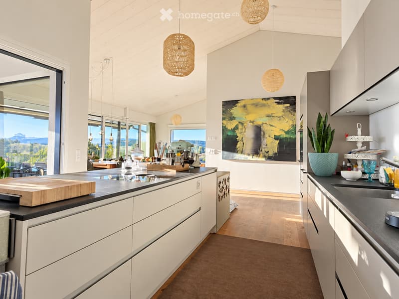 Modern kitchen with white cabinets, dark countertops, pendant lights, and a view of the outdoors.