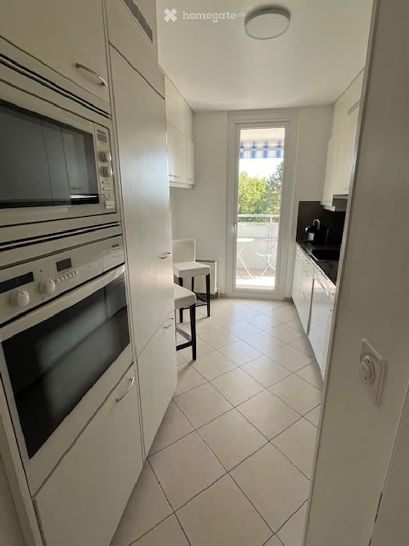 Modern kitchen with white cabinets, stainless steel appliances, tiled floor, and access to a balcony.