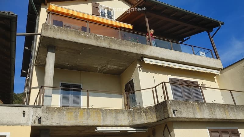 Two-story residential building with balconies, shutters, and awnings.