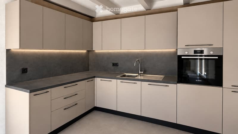 Modern kitchen with light-colored cabinets, dark countertops, and built-in appliances including a sink and oven.