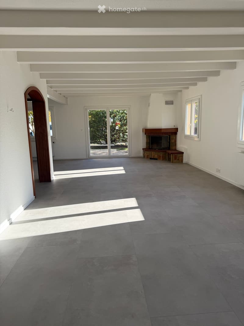 Empty room with grey tiled floor, white walls, and a fireplace with wooden mantel. Large sliding glass door leads to outdoor area.
