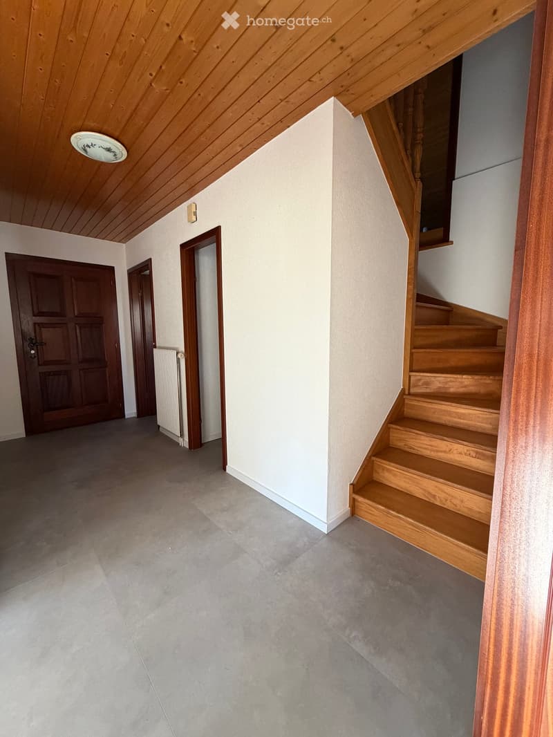 Empty hallway with wooden staircase, wooden doors, and a radiator on the wall.