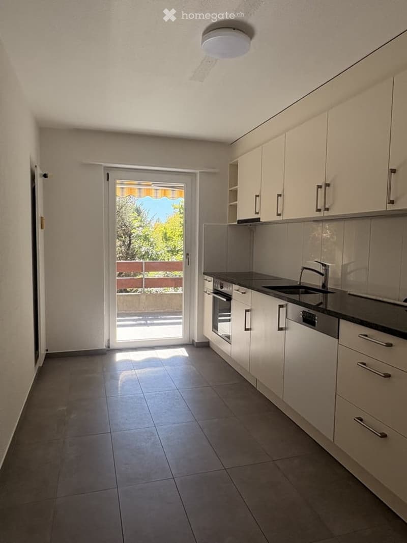 Modern kitchen with white cabinets, dark countertops, and a sliding glass door leading to a balcony. Features include a sink, faucet, oven, and dishwasher.