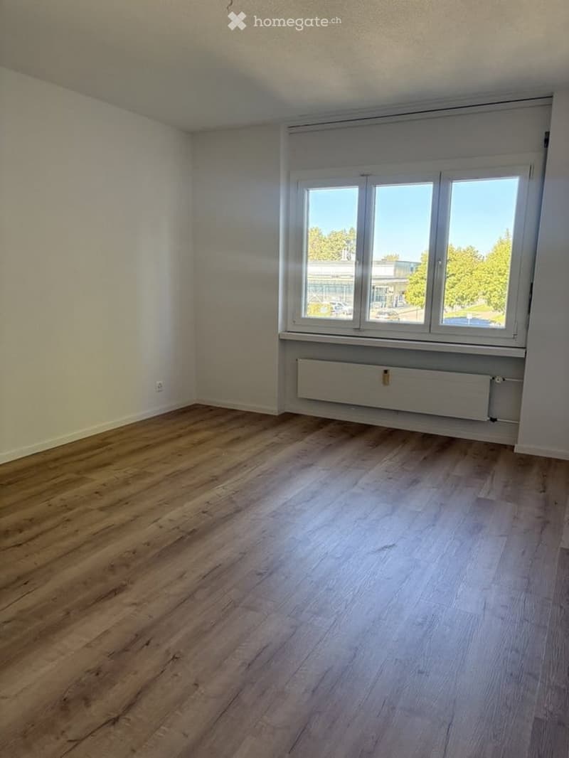 Empty room with wooden flooring, white walls, and large windows offering a view of the outside. No furniture or equipment present.