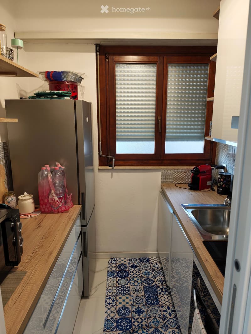Compact kitchen with wooden countertops, stainless steel sink, refrigerator, microwave, coffee maker, and various small items on the counters.