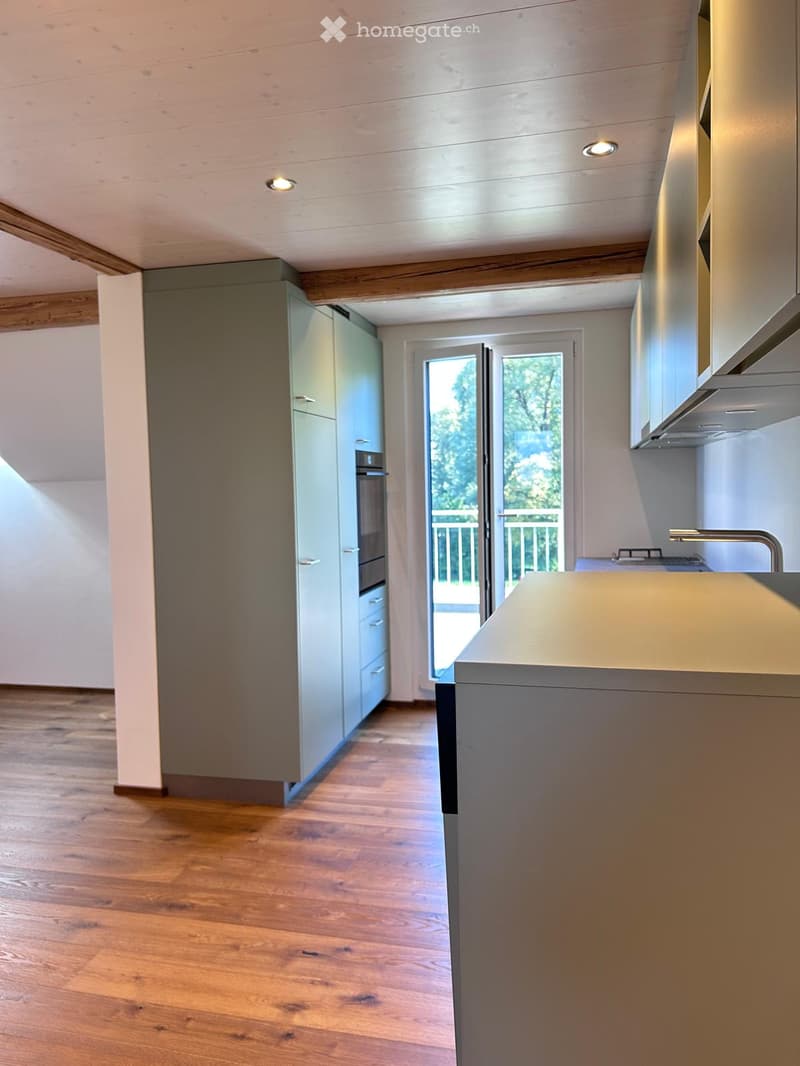Modern kitchen with light grey cabinets, wooden flooring, and a view of the outdoor area through large glass doors.