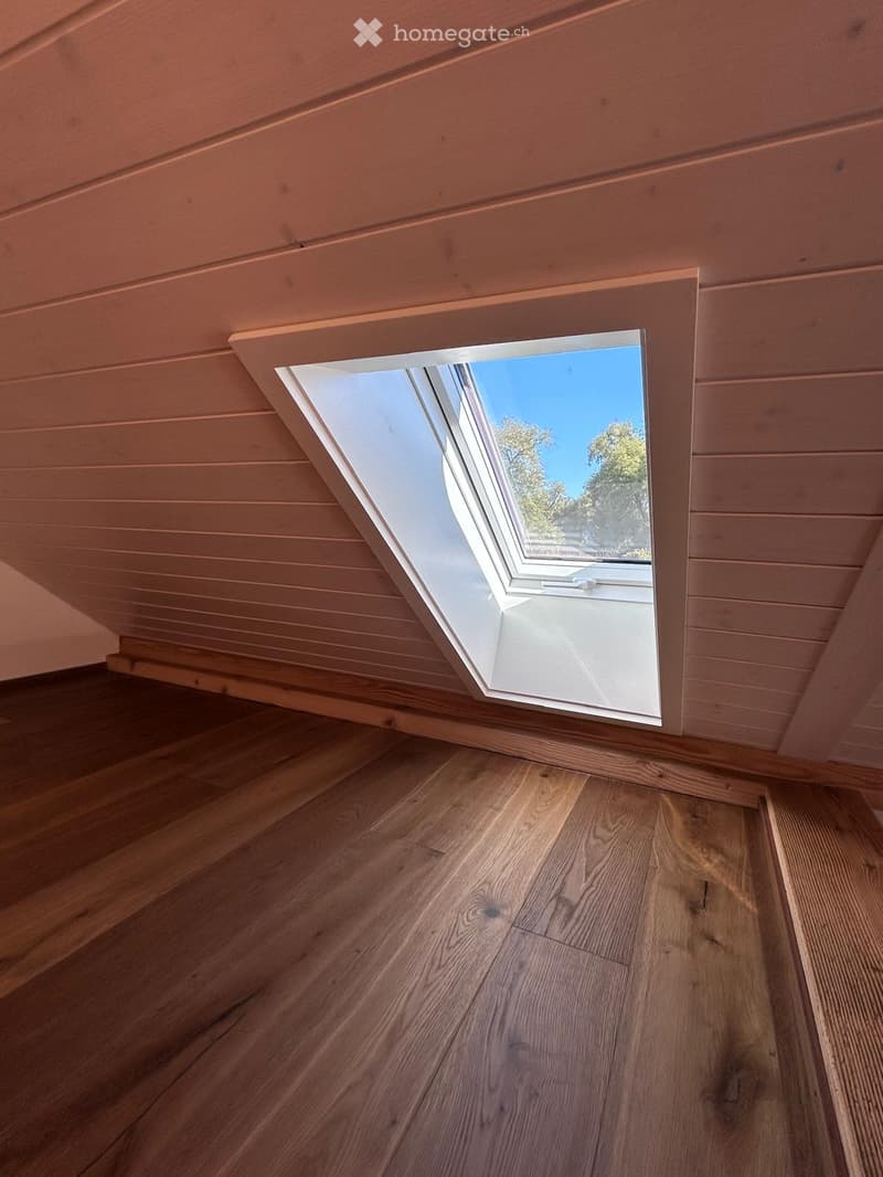 An unfurnished room with wooden flooring and a skylight window offering a view of the outdoors.