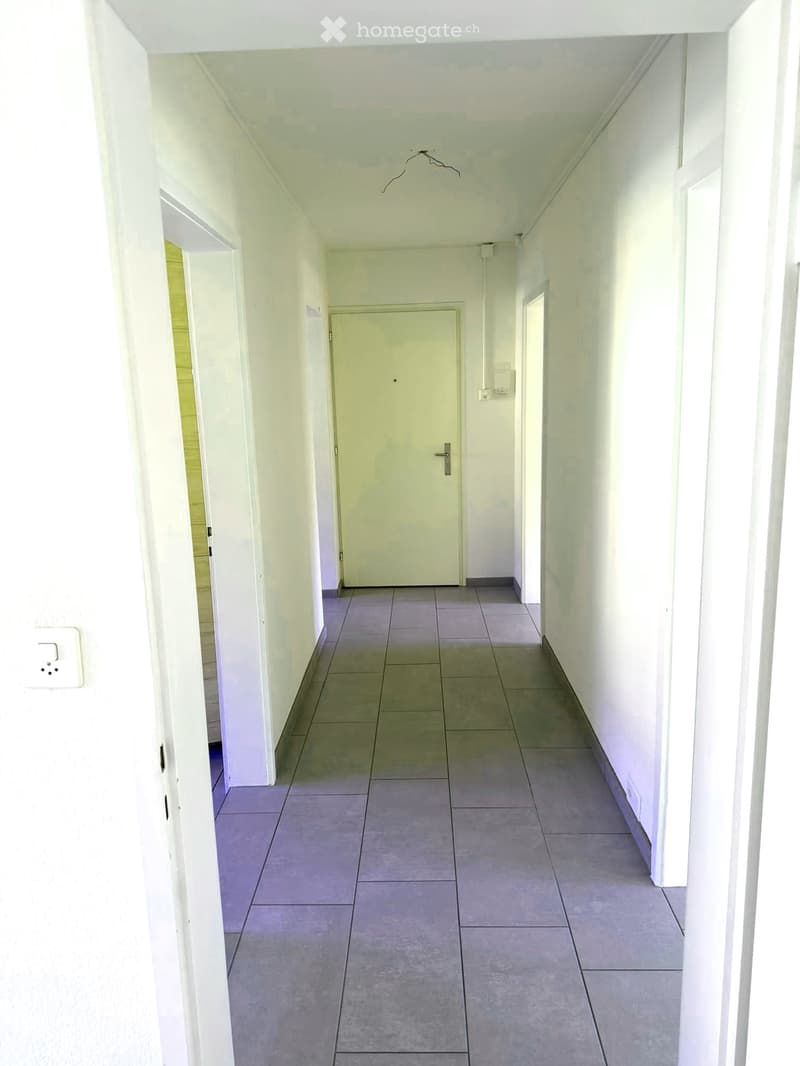 Empty hallway with tiled floor, white walls, and a closed door at the end.