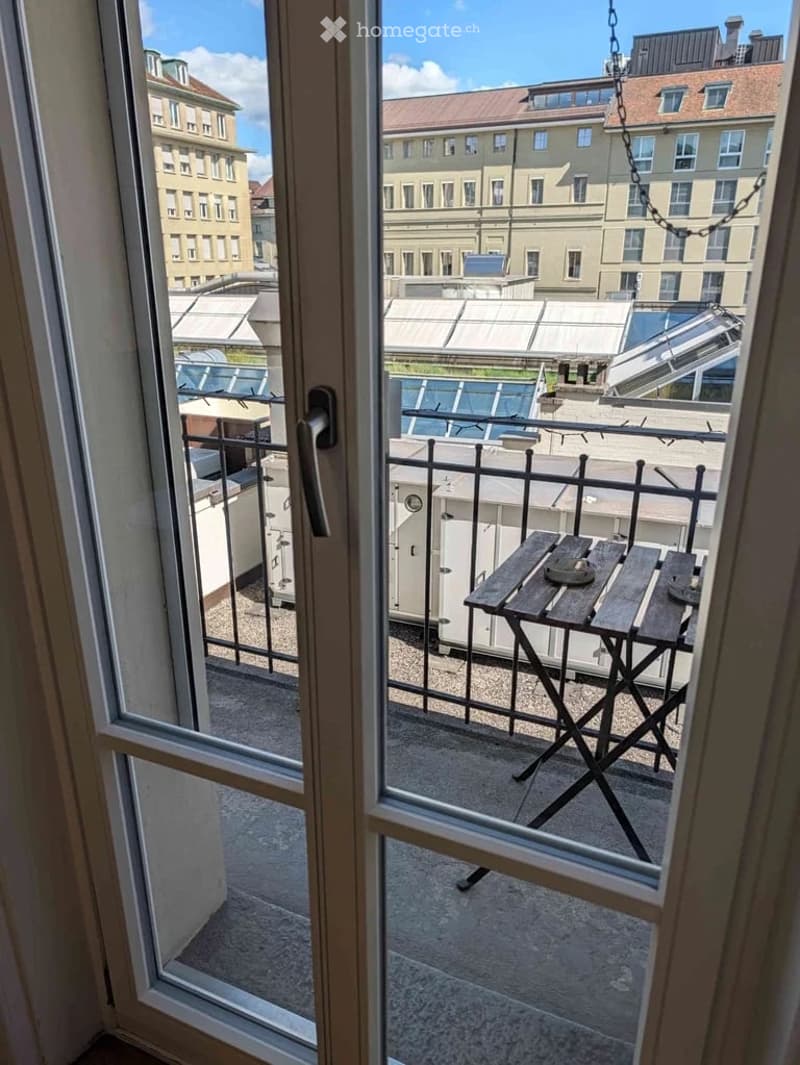 Balcony with a view of the city, featuring a single wooden chair and a small table.