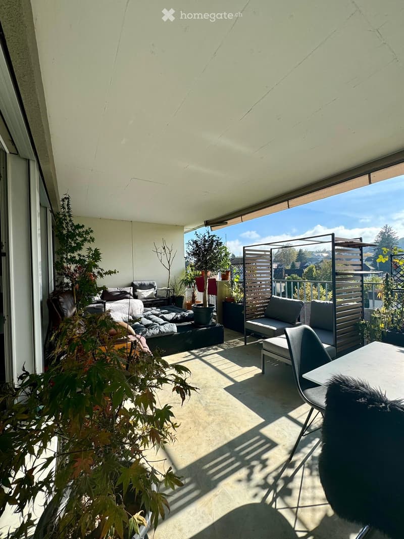 Modern balcony with a view, featuring a sofa, chairs, a table, and potted plants.