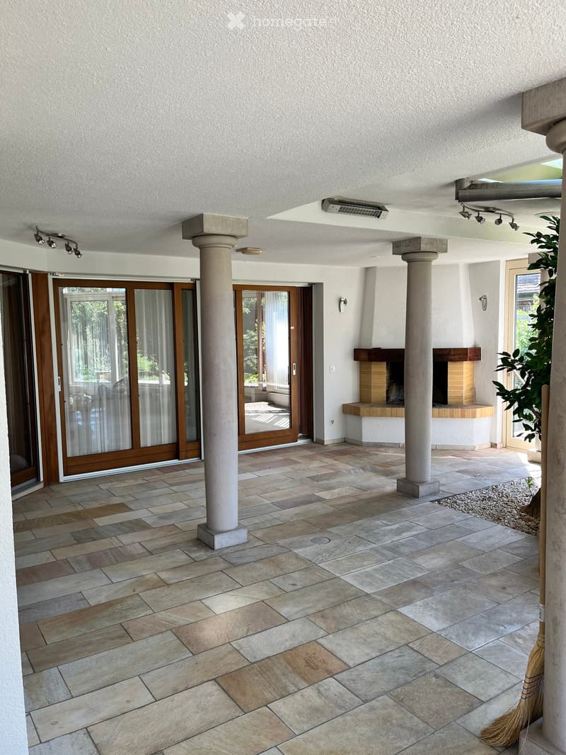 Open patio area with tiled flooring, two large columns, a built-in fireplace, and large glass doors leading to the interior.
