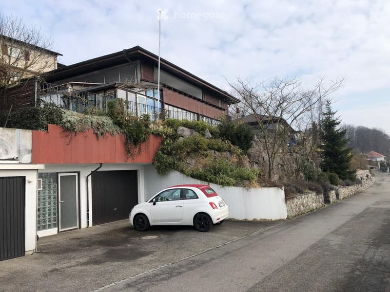 Two-story house with a balcony, garage, and a small white car parked in front.