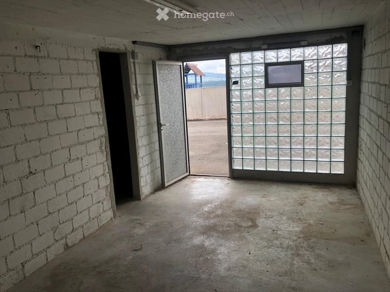 Empty room with exposed brick walls, concrete floor, and two open doors leading to an outdoor area.
