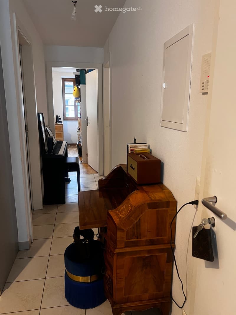 Hallway with tiled floor, wooden cabinet, piano, and a small table with a box on top.