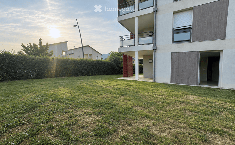 Lush green lawn in front of a modern multi-story building with balconies and wooden shutters.