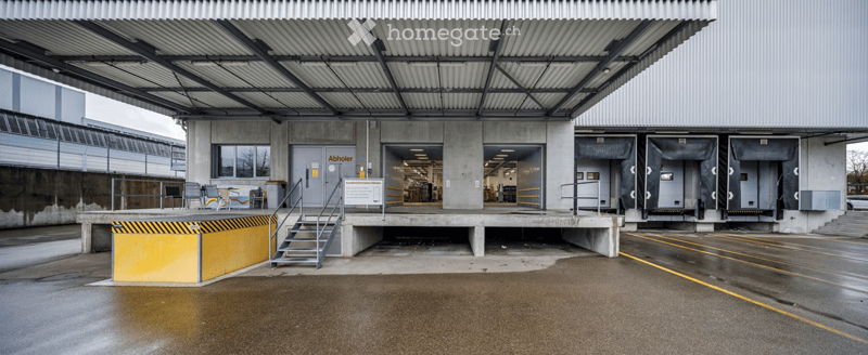 Modern industrial-style building with a large covered entrance, concrete structure, and multiple loading bays.