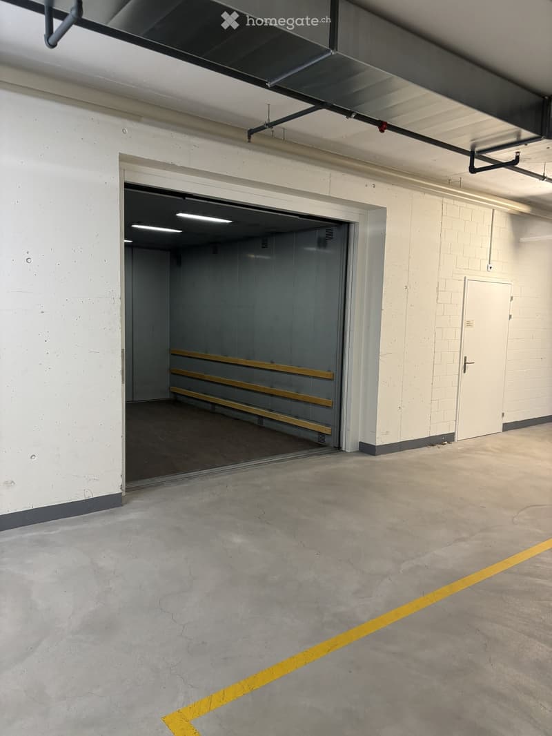 Empty underground parking area with concrete floors, white brick walls, and a large open garage entrance.