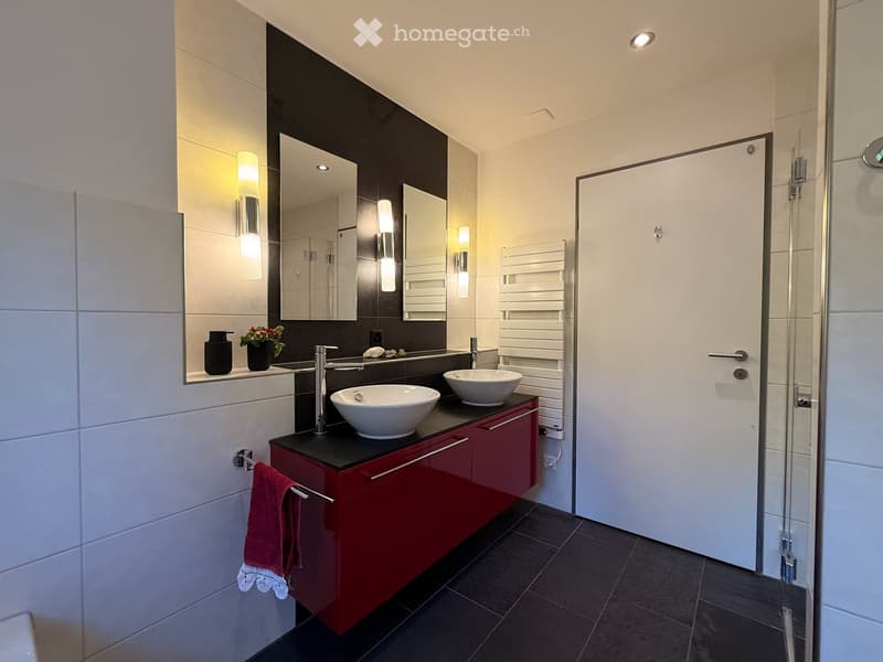 Modern bathroom with two white sinks, red cabinetry, black countertop, large mirror, and a glass shower enclosure.