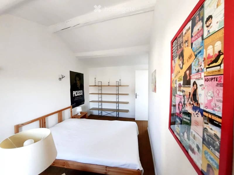modern bedroom with wooden bed, white sheets, wooden nightstand, white lamp, framed posters, shelf, white walls, wooden floors