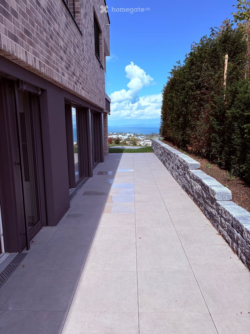 A paved pathway leading to a modern building with large windows, overlooking a scenic ocean view.