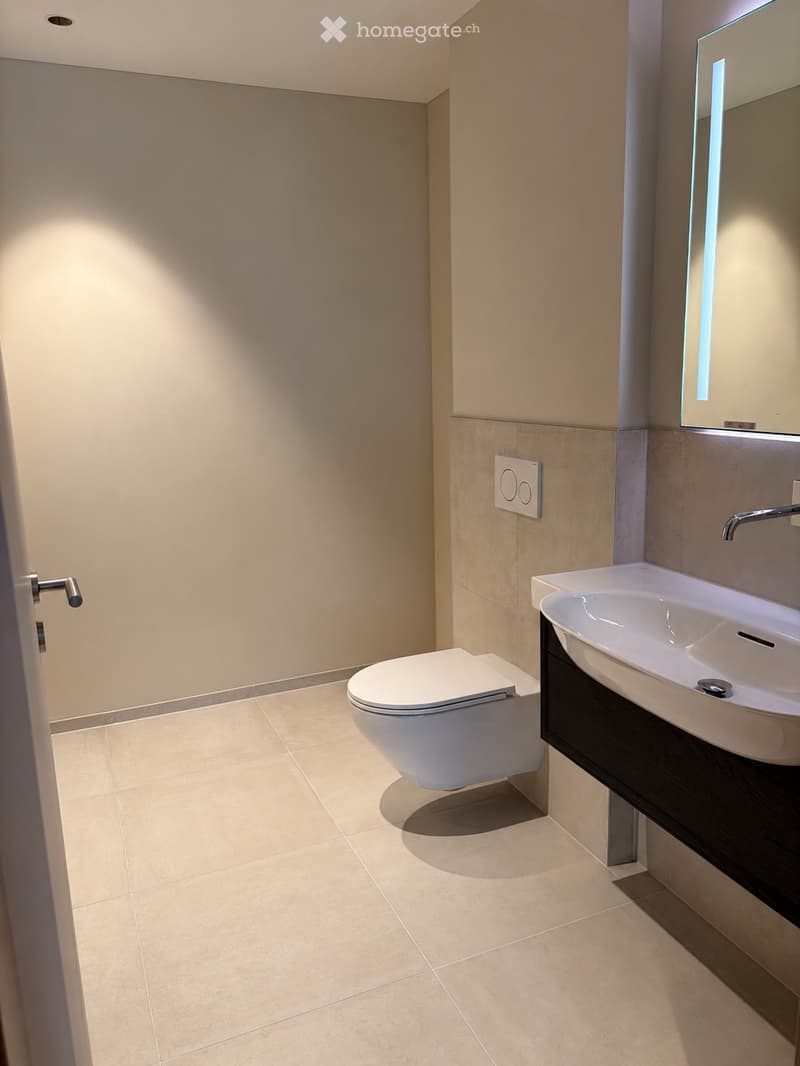 Modern bathroom with beige tiles, a white toilet, a sink with a modern faucet, and a large mirror above the sink.