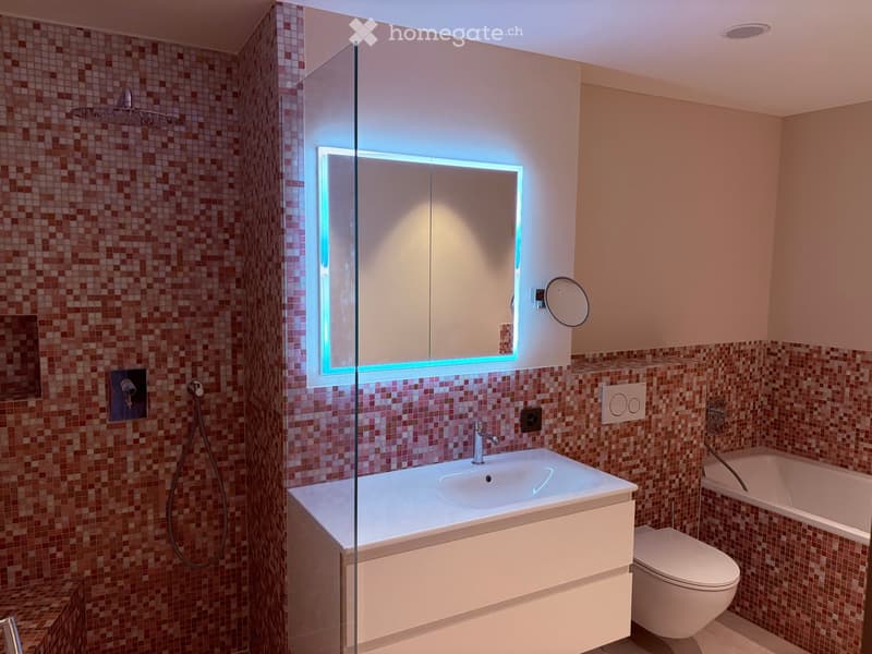 Modern bathroom with a white sink, mirror with LED lighting, toilet, bathtub, and a glass-enclosed shower area with a rainfall showerhead.