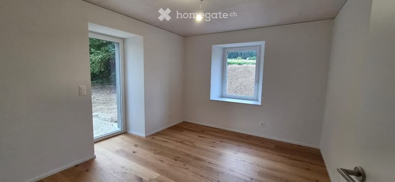 Empty room with wooden flooring, white walls, and two windows, one of which is a sliding glass door leading outside.