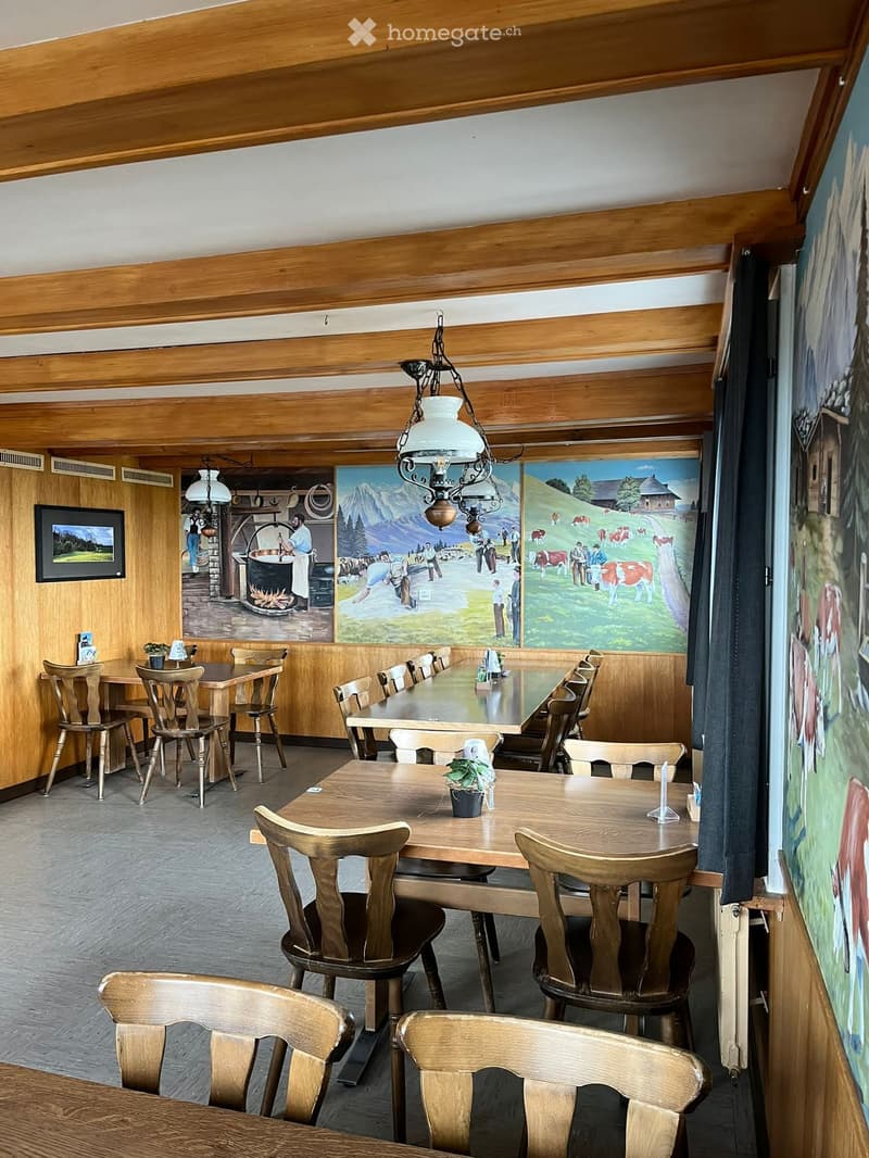 A cozy restaurant or dining area with wooden tables and chairs, a hanging pendant light, and large murals on the walls.