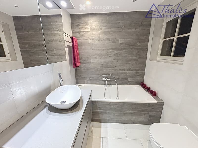 Modern bathroom with a bathtub, sink, toilet, and a towel hanging on the wall. The walls are tiled in a wood-like pattern, and the floor is tiled in white.